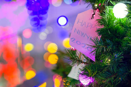 Paper hanging on Christmas tree for Holiday decoration with colorful lights on background.