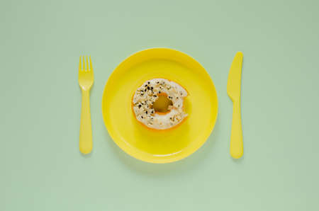 Bited donut on yellow plate wtih knife and fork on green background. Minimal creative unhealthy food concept.の写真素材