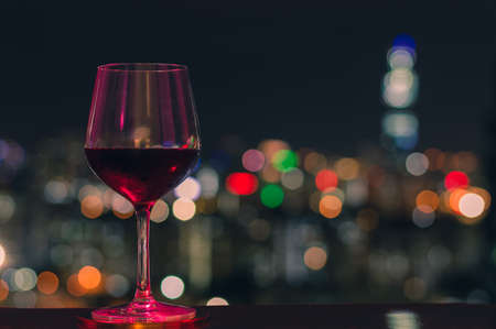 Colorful light shine on a glass of red wine with colorful bokeh of city lights.の写真素材