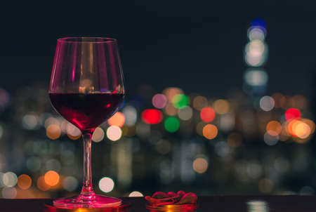 Colorful light shine on a glass of red wine and olives with colorful bokeh of city lights.の写真素材