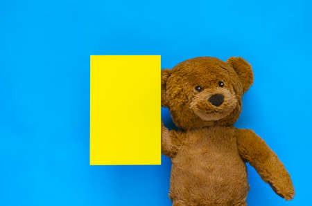 A cute brown teddy bear holding a blank yellow note with blue background for April fools day concept.の写真素材