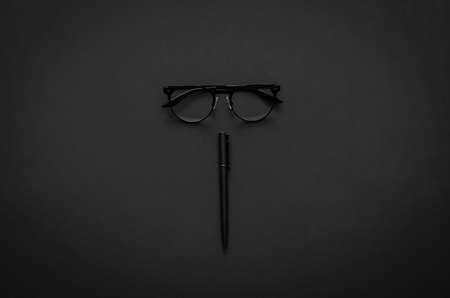 Eyeglasses and pen in modern lifestyle on dark background for minimalist flat lay black concept. の写真素材