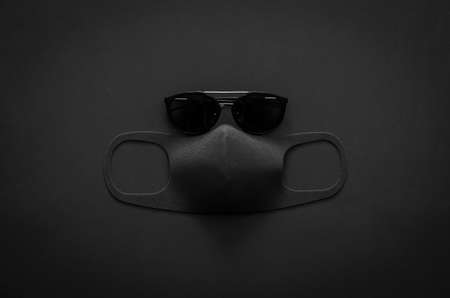 Sunglasses and face mask to protect virus on dark background for minimalist flat lay black concept.の写真素材