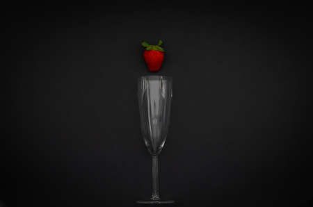 Strawberry and wineglass on dark background for minimalist flat lay black food and drink concept.の写真素材