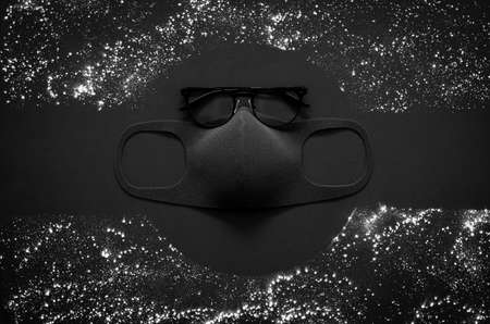 Eyeglasses and face mask to protect virus with white dust on dark background for flat lay black concept.の写真素材