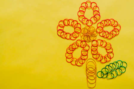 Colorful elastic rubber bands set in flower shape put on yellow background with empty space for...