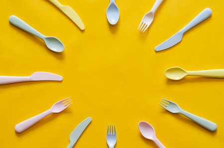Colorful fork, spoon and knife on yellow background with empty space for text in the middle.