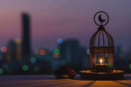 Lantern that have moon symbol on top and small plate of dates fruit with dusk sky and city bokeh...