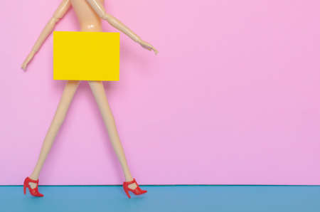 Naked female doll walking with red shoe with yellow paper hiding the bottom area. Minimal beauty and sexually harassment concept.の写真素材