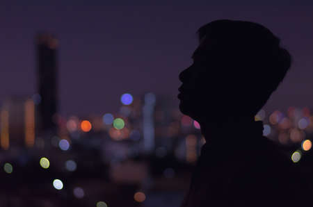 A man standing in darkness alone looking to somewhere with colorful city bokeh lights as background....