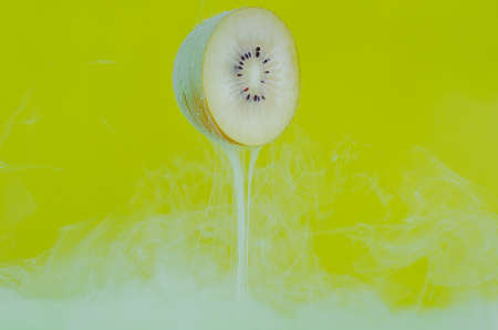 Blurred focus of dissolving green poster color in water with slice kiwi fruit on yellow background...