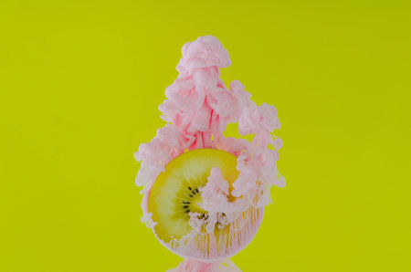 Slice kiwi fruit with partial focus of dissolving pink poster color in water on yellow background for summer, abstract and background concept.の写真素材