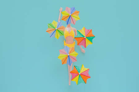 A doll wearing yellow swimming suit with cocktail umbrellas on blue background. Minimal summer concept.の写真素材