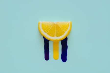 Slice lemon that have yellow and dark blue poster color drop from it with blue background. Minimal summer concept.の写真素材