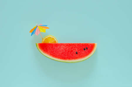 Red watermelon with slice lemon and cocktail umbrella on blue background. Minimal summer drink concept.の写真素材