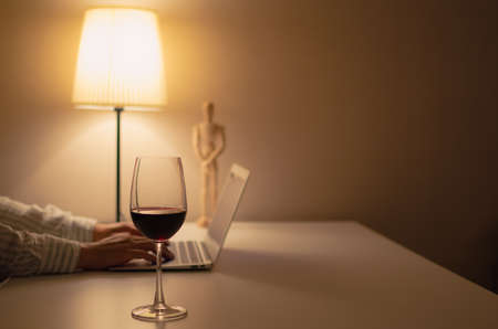 A glass of red wine puts on table to drink and relax when working at home.の写真素材