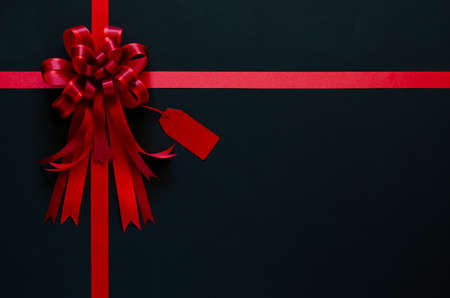Red ribbon with bow and price tag on black background. Black friday concept.の写真素材