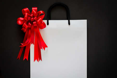 White shopping bag with red bow and ribbon on black background. Black friday concept.の写真素材