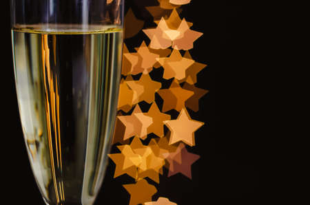 Blurred focus of a glass of sparkling wine with white bubble and star shape golden bokeh lights on dark background.の写真素材