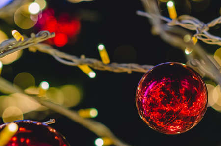 Red bauble on Christmas tree with colorful bokeh lights background.