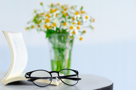 Spectacles puts on a book with blurred flowers background.の写真素材