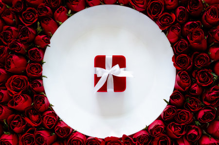 Red gift box on white plate with roses background for dinning on anniversary or Valentine's day concept.の写真素材