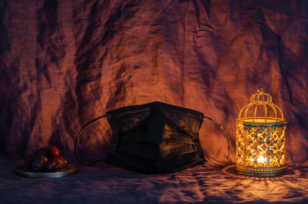 Black face mask, golden lantern and dates fruit on dark background for the Muslim feast of the holy month of Ramadan Kareem.の写真素材