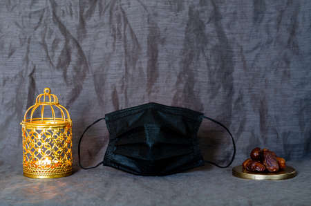 Black face mask, golden lantern and dates fruit on cloth background for the Muslim feast of the holy month of Ramadan Kareem.の写真素材