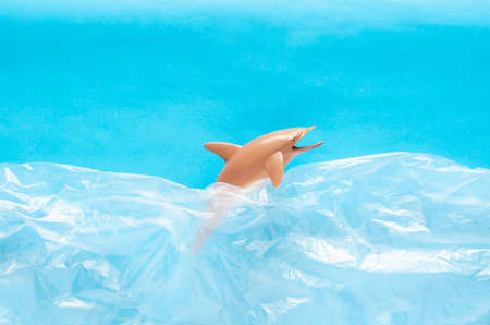 A dolphin toy model trapped in white plastic bag on blue background. Minimal ocean world concept.の写真素材