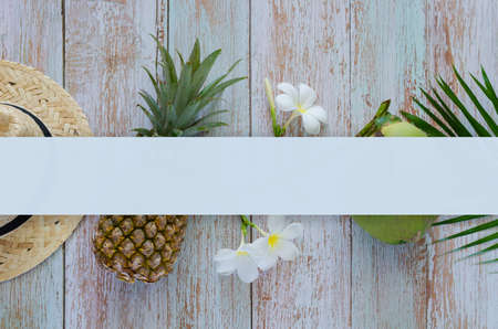 Summer background concept with beach hat, pineapple, coconut, frangipani flowers on blue wooden background with blank space for text.の写真素材