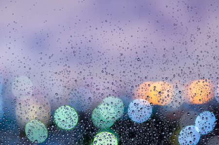 Rain drop on glass window in monsoon season with colorful bokeh light from city buildings background.の写真素材