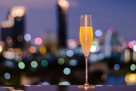 A glass with vapour of cold Champagne on table with colorful city bokeh lights background.の写真素材