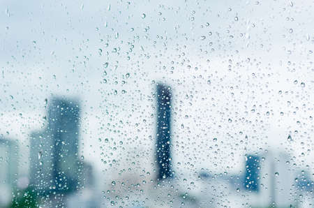 Rain drop on glass window at day time in monsoon season with blurred city buildings background.の写真素材