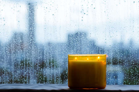 Burning aroma candle puts near by window that have rain drop in monsoon season. Zen and relax concept.の写真素材