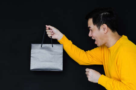 Asian happy male holding shopping bags on dark background for Black Friday concept.の写真素材