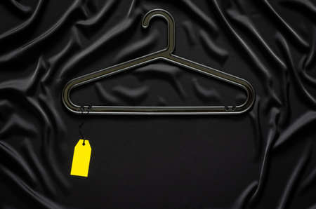 A black hanger with blank yellow price tag on black smooth and wavy cloth with space for text. Black Friday concept.の写真素材