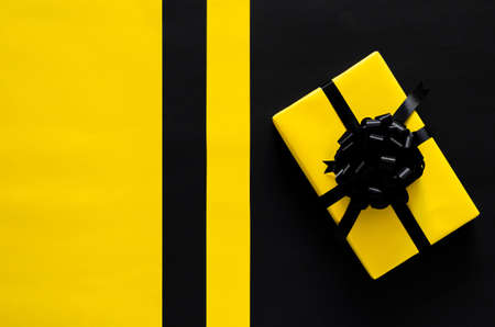 A yellow gift box with black ribbon puts on black and yellow background. Black friday and Boxing day concept.の写真素材