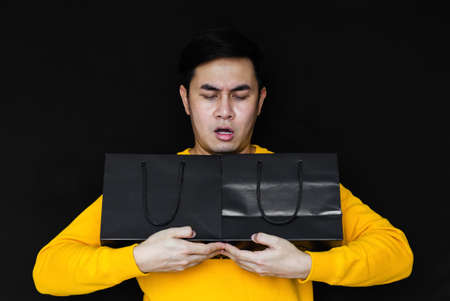 Asian male acting amaze and holding shopping bags on dark background for Black Friday concept.の写真素材