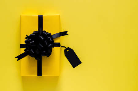 A yellow gift box with black ribbon and blank price tag puts on yellow background. Black friday and Boxing day concept.の写真素材