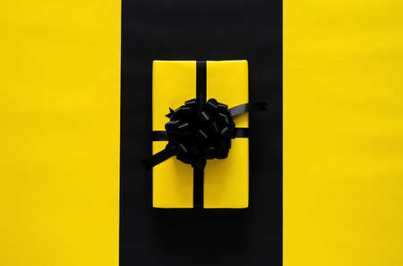 A yellow gift box with black ribbon puts on black and yellow background. Black friday and Boxing day concept.の写真素材