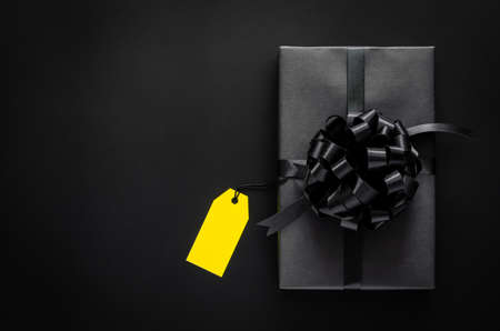 A black gift box with ribbon and yellow blank price tag puts on black background. Black friday and Boxing day concept.の写真素材