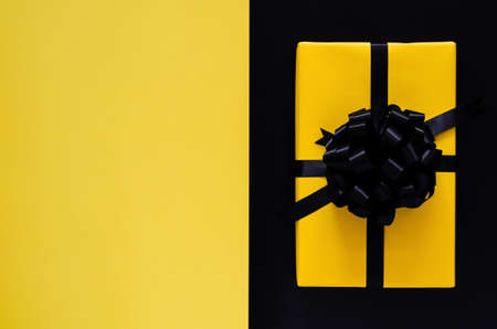 A yellow gift box with black ribbon puts on black and yellow background. Black friday and Boxing day concept.の写真素材