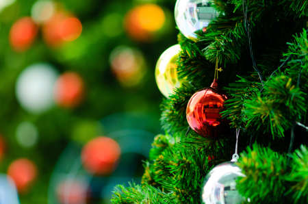 Red bauble and other ornament hanging on Christmas tree with bokeh background from another bigger Christmas tree.の写真素材