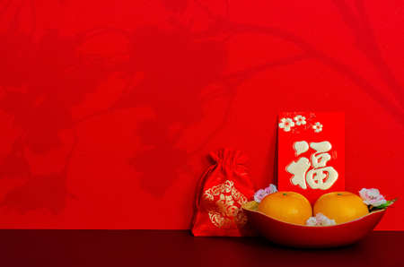Red envelope packet or ang bao (word mean wealth) puts with oranges and red bag (word is wealth) with shadow of peach blossom on red glitter paper background.の写真素材