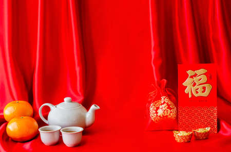 Chinese new year background with red envelope packets or ang bao(word means wealth) ingots, red bag (word means wealth), tea set and oranges on red satin cloth background.の写真素材
