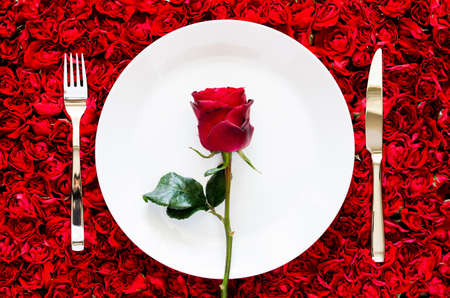 Red rose put on white plate with knife and fork on red rose background for dining, anniversary and Valentine's day concept.の写真素材