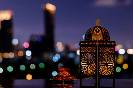 Lantern and small plate of dates fruit with night sky and city bokeh light background for the Muslim feast of the holy month of Ramadan Kareem.の写真素材