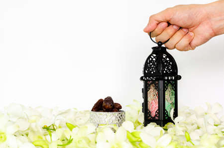 Hand holding lantern on white background with dates fruit on orchid flower for the Muslim feast of the holy month of Ramadan Kareem.の写真素材