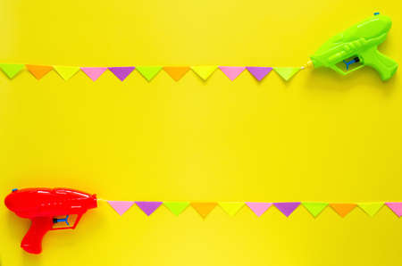 Two water gun spray out with colorful party flag for Songkran festival celebration on yellow color background. Minimal holiday concept.の写真素材