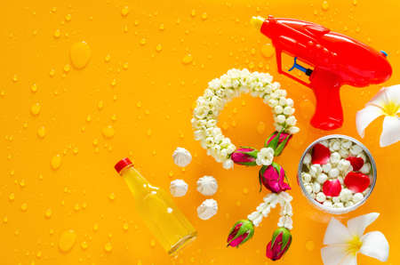 Songkran festival background with jasmine garland, water gun, flowers in water bowl, scented water and marly limestone put on clear mirror that have wet yellow background below.の写真素材